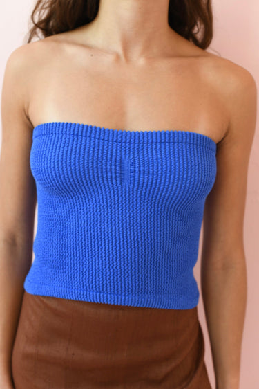 Blue strapless top worn by a person on a pink background