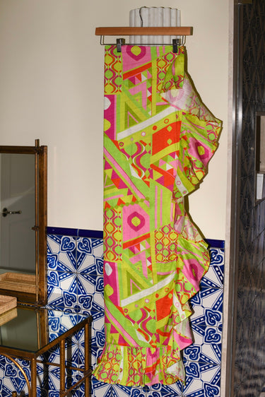 Colorful patterned ruffle power pareo skirt hanging against a wall with a tiled base.