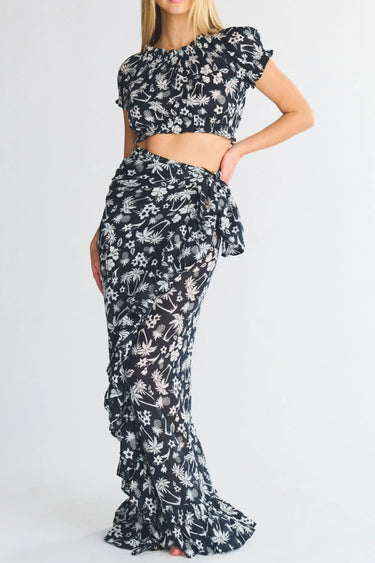 Woman wearing a black and white palm tree patterned crop top and ruffle power pareo skirt on a white background