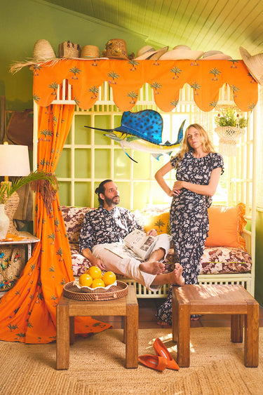 Man and woman in matching palm tree black and white patterned outfits in a colorful room. 