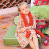 Young girl in a colorful dress sitting on a green cushion outdoors.
