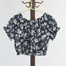 Black and white palm tree patterned crop top on a hanger against a white background