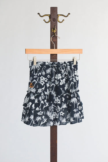 Black and white floral and palm tree patterned mini skirt hanging on a wooden hanger against a white background