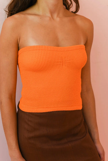 Orange strapless top worn by a person on a pink background