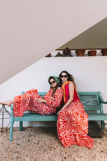 Two women in red and white patterned outfits sitting on a green bench.