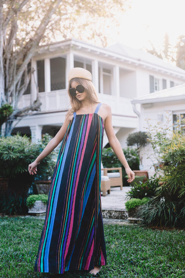 Woman in a colorful striped dress standing outdoors with a house in the background