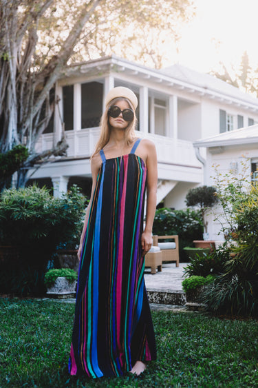 Woman in a colorful striped dress standing in a garden with a house in the background
