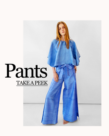 A model stands barefoot in a studio wearing wide-leg periwinkle pants with a matching cricket flutter sleeve top. Large text on the left reads 'Pants TAKE A PEEK'. Click on the image to be taken to the pants collection.