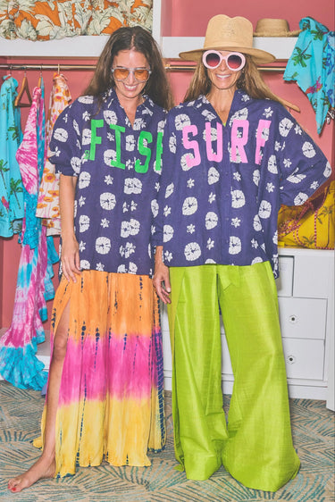 Two people wearing navy printed button down shirts with text and patterns, standing in a room with clothing racks.