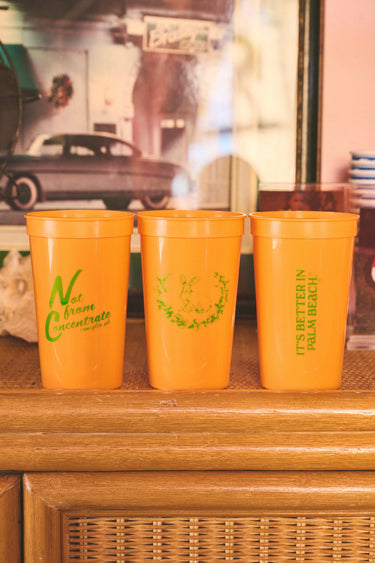 3 orange cups on a rattan cabinet with the Coniglio Palm Beach logo.