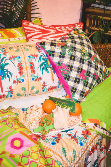 Colorful pillows and a blanket with various patterns on a bed with Get in we're going to Palm Beach bumper stickers.