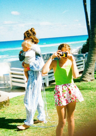 A child taking a photograph wearing a patterned mini skirt near the ocean.