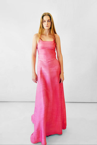 A woman modeling a bright pink sleeveless top with a fitted bodice and flowing skirt, standing against a plain light gray studio background.